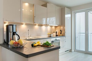 A modern kitchen with a central island, stainless steel appliances, and a view to the outside. - Kurparkresidenz Apartment 16 - Kurparkresidenz (Scharbeutz)