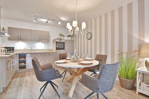 Una cocina moderna con comedor, que presenta una mesa redonda con sillas, una araña y papel tapiz a rayas.
