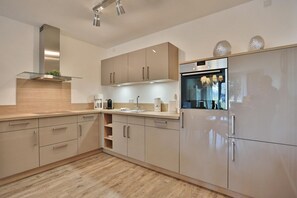 Una cocina moderna con armarios de madera clara, electrodomésticos de acero inoxidable y horno empotrado.