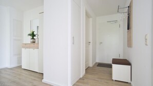 Un pasillo moderno y minimalista con suelo de madera, paredes blancas y un pequeño banco.