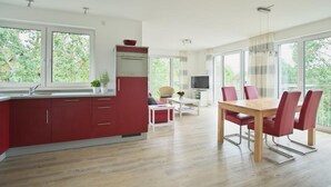 Una cocina moderna con armarios rojos, un comedor con mesa y sillas de madera, todo ello con grandes ventanales que ofrecen vistas a la vegetación.
