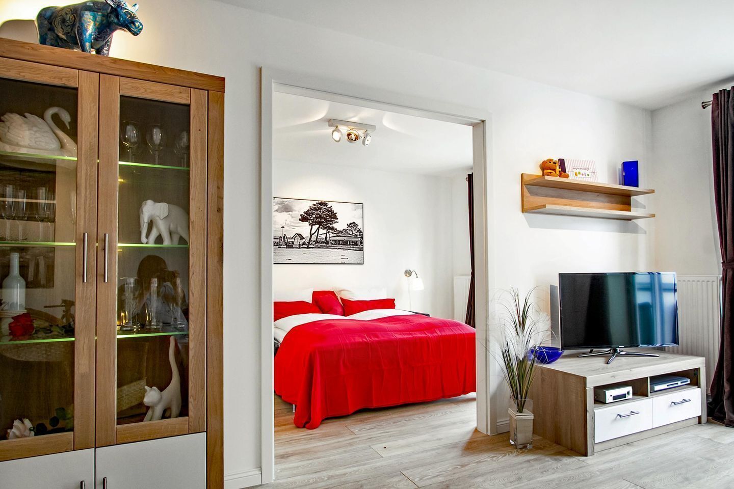 Ein modernes Schlafzimmer mit roter Bettdecke, einem Fernseher und einem Schrank mit Glastüren.