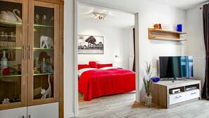 A modern bedroom with a red bedspread, a TV, and a cabinet with glass doors.