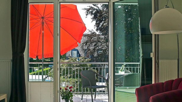A room with a sliding glass door leading to a balcony, a red chair, and a red sofa.