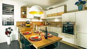 A modern kitchen with white cabinets, a wooden dining table set for four, and a large pendant light.