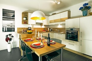 Una cocina moderna con armarios blancos, una mesa de comedor de madera para cuatro comensales y una lámpara colgante grande.