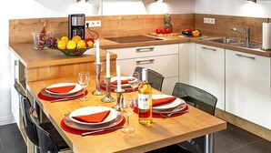 A modern kitchen with a wooden dining table set for four, equipped with a coffee maker, a fruit bowl, and a wine bottle.