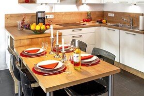 Una cocina moderna con una mesa de comedor de madera para cuatro personas, equipada con una cafetera, un frutero y una botella de vino.
