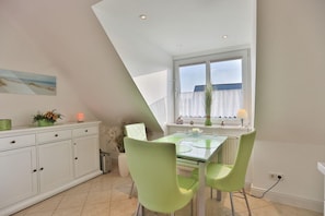 A modern kitchen with a dining area, featuring a table with chairs, a window with curtains, and a ceiling with recessed lighting. - Hansa-residenz I Appartement 17 Kumweer - Hansa-residenz I (Scharbeutz)
