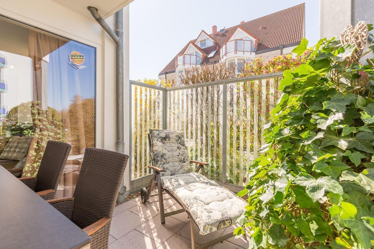 Eine Außenpatio mit Korbmöbeln, einem Metallzaun und Blick auf ein Wohngebäude im Hintergrund.