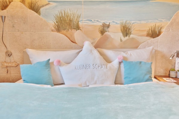 A bed with a beach-themed mural in the background, a sign reading "BEACH", and a pillow with "KLEINER SCHATZ".