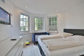 A modern bedroom with two beds, large windows, a radiator, and a desk with a computer. - Vacation apartment Ostseehöhe Apartment 1 - Holiday home Glockenstraße (Scharbeutz)