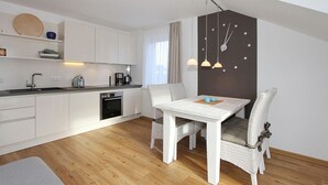 Eine moderne Küche mit weißen Schränken, einem eingebauten Ofen und einem Essbereich mit weißem Tisch und Korbstühlen.