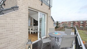 Ein Balkon mit Tisch und Stühlen, Holzboden und Blick auf benachbarte Gebäude.