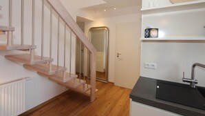Eine moderne Küche mit einer Holztreppe, einer schwarzen Arbeitsplatte und einer weißen Wand mit Regal.