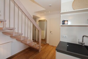 Una cocina moderna con una escalera de madera, una encimera negra y una pared blanca con un estante.