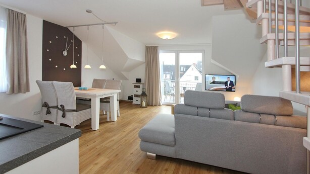 Ein modernes Apartment mit Essbereich, einem grauen Sofa, einem Fernseher und einer Treppe.