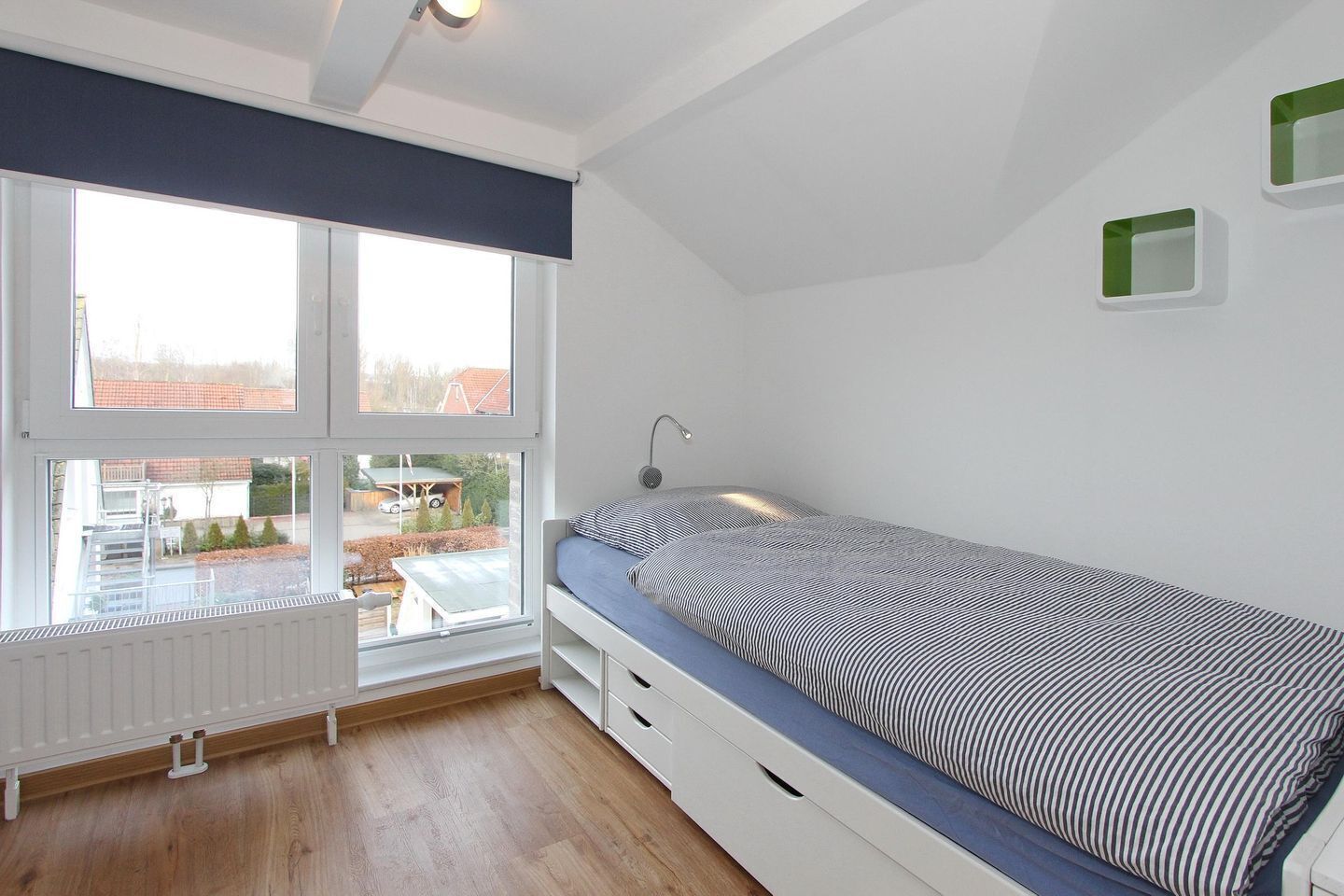 A bedroom with a single bed, a window with blinds, a radiator, and a view of the outside.