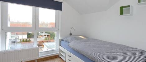 A bedroom with a single bed, a window with blinds, a radiator, and a view of the outside.