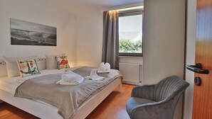 A hotel room with a bed, a chair, a window with curtains, and a radiator.