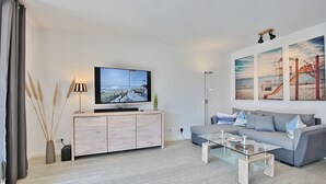A modern living room with a flat-screen TV, a grey sofa, a glass coffee table, and a wooden cabinet.