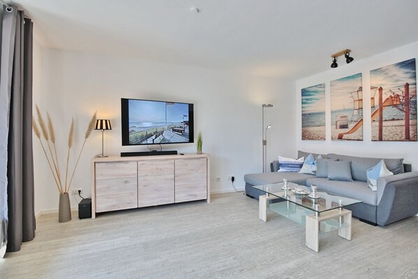 A modern living room with a flat-screen TV, a grey sofa, a glass coffee table, and a wooden cabinet.