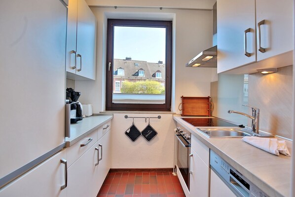 A compact kitchen with white cabinets, a window, a built-in oven, and a sink.