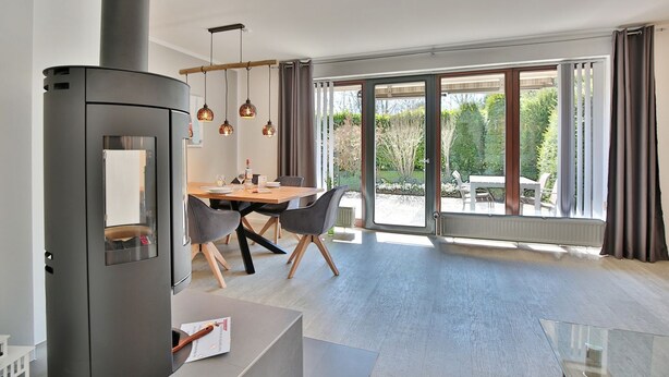 A modern kitchen with a built-in stove, a dining area with a wooden table and chairs, and large sliding glass doors leading to an outdoor patio.