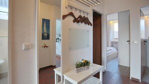 A hotel room with a bed, a small table with a vase, a mirror, and a coat rack.