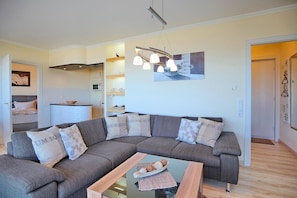 A modern living room with a grey sectional sofa, a glass coffee table, and a contemporary pendant light.