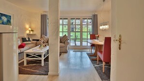 Un salon chaleureux avec un canapé, une table à manger et une vue sur l’extérieur grâce à de grandes fenêtres.
