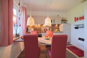 A modern kitchen with white cabinets, a dining area with red chairs, and pendant lights.