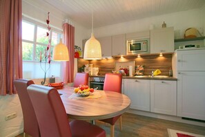 A modern kitchen with white cabinets, a microwave, and a sink. There is a dining table with chairs and a fruit bowl on it.