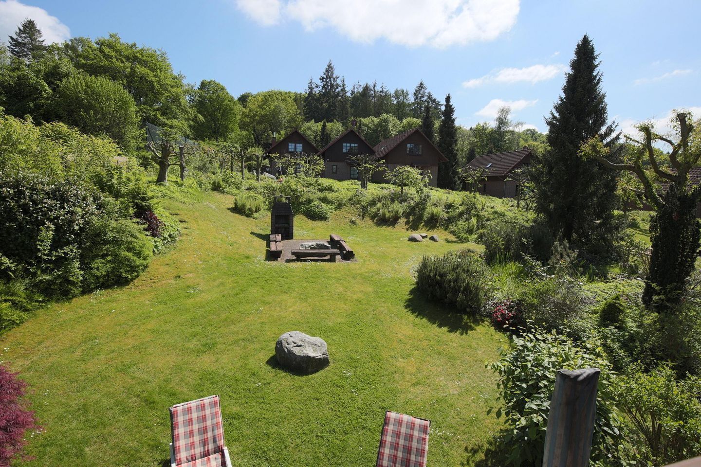 A grassy backyard with a barbecue area, two chairs, and a stone.
