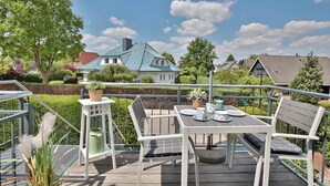 Una terraza con una mesa dispuesta para tomar té, rodeada por una barandilla de metal, con vistas a casas y árboles al fondo.