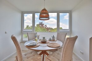 Un comedor con una mesa redonda, sillas de mimbre y una lámpara colgante.