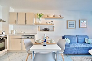 Uma cozinha moderna com área de refeições, com uma mesa branca, cadeiras e um sofá azul.
