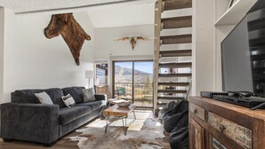 Een woonkamer met een grijze bank, een houten salontafel, een leren divan, een houten kast en een opgeplakt dierenhoofd.