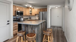 Een moderne keuken met houten kastjes, roestvrijstalen apparatuur, een granieten aanrecht en drie houten barkrukken.