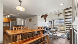 Een ruime woonkamer met een houten eettafel, een bank en een groot raam met uitzicht op bergen.