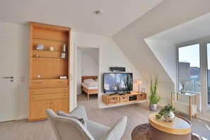 A modern living room with a TV, a sofa, a coffee table, and a large wooden cabinet. - Hansa Residence II Apartment 25 - Hansa Residence II (Scharbeutz)
