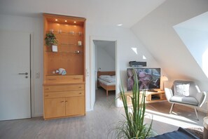 A modern bedroom with a sloped ceiling, a wooden wardrobe, a bed, a TV, and a chair. - Hansa Residence II Apartment 25 - Hansa Residence II (Scharbeutz)