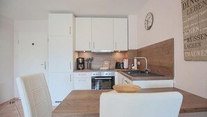 A compact kitchen with white cabinets, a wooden countertop, a sink, and a dining area with a table and chairs.
