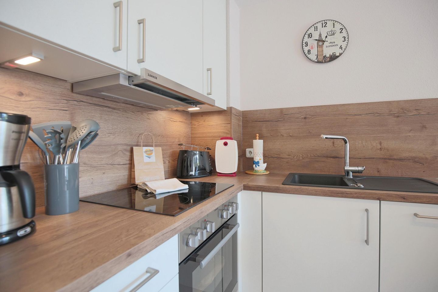 Een moderne keuken met een houten achterwand, roestvrijstalen apparatuur en een wandklok.