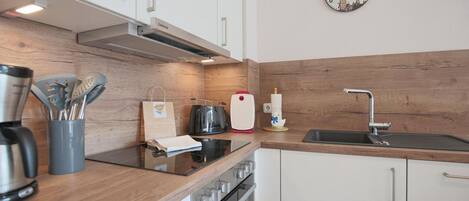 Een moderne keuken met een houten achterwand, roestvrijstalen apparatuur en een wandklok.