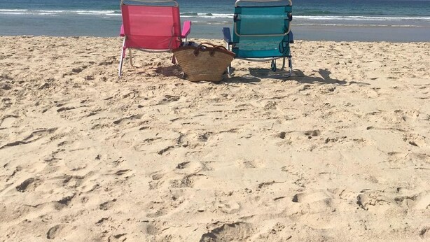 Two beach chairs on a sandy beach with the ocean in the background.