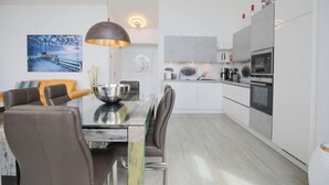 A modern kitchen with white cabinets, a dining area with a glass table, and a pendant light.