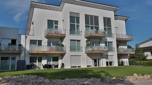 A modern multi-story residential building with balconies, a paved driveway, and a well-maintained lawn.