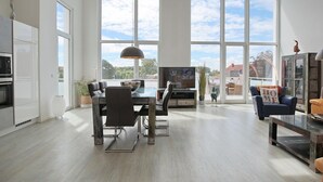 A spacious living room with a large dining table, comfortable seating, a television, and a view of the outdoors through large windows.
