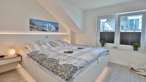 Ein Schlafzimmer mit Bett, Nachttisch, Lampe und einem Fenster mit Jalousien.